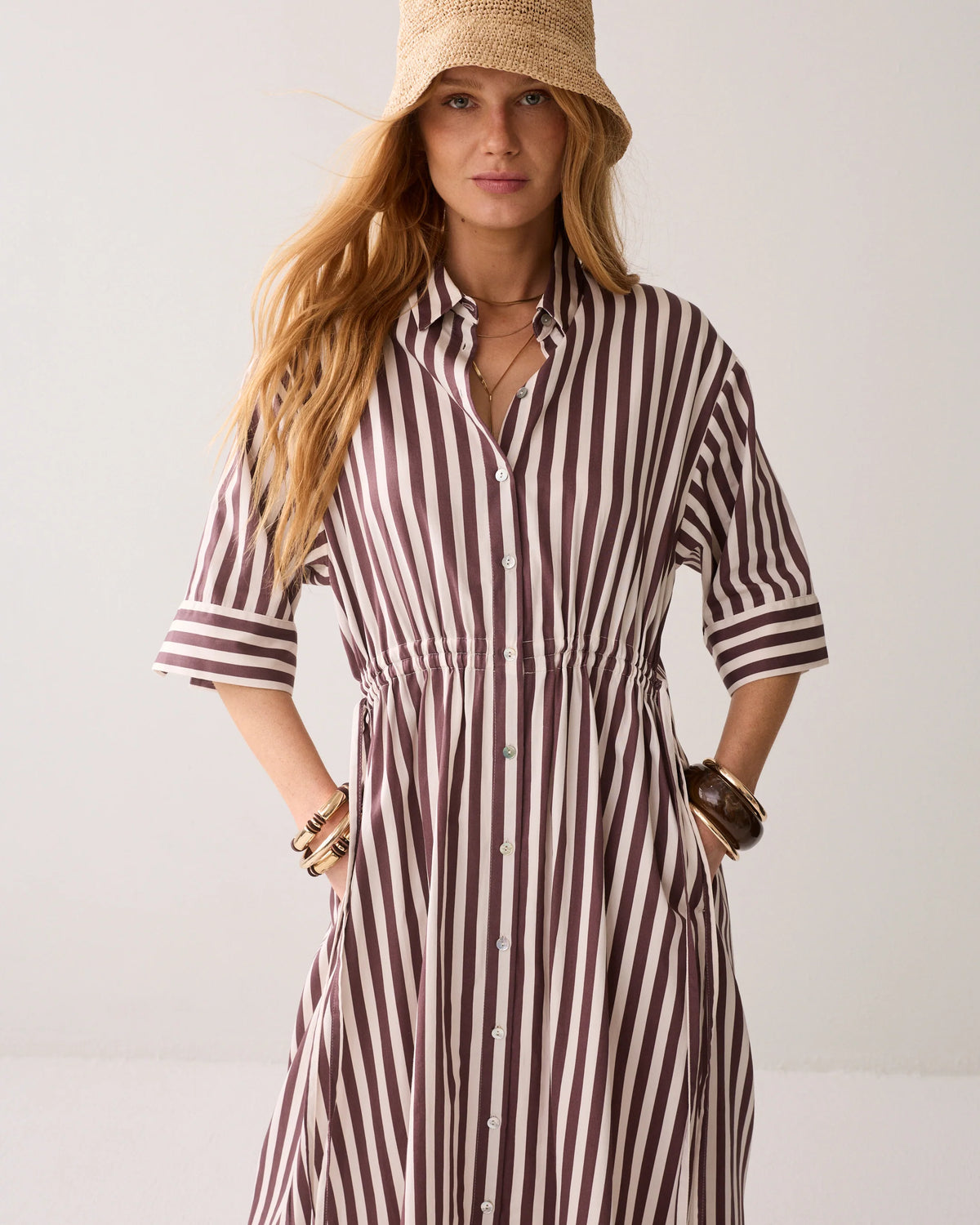 Woman wearing a striped dress and straw hat against a plain background