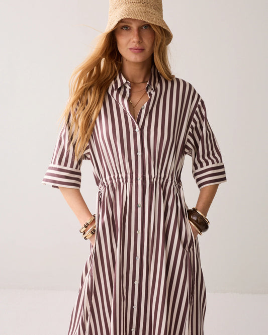 Woman wearing a striped dress and straw hat against a plain background